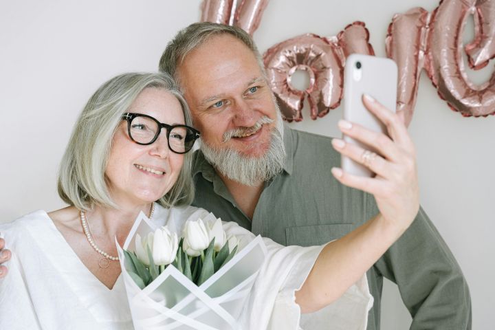 Happy senior couple taking a selfie with a bouquet of tulips, celebrating love.