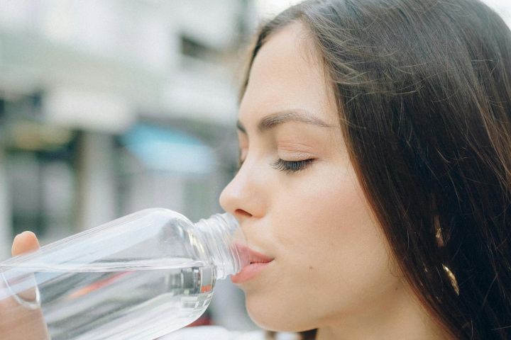 Side view of a young woman drinking water from a bottle in an outdoor setting.