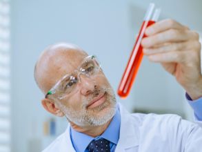 Scientist carefully examining red liquid in test tube in a lab setting.
